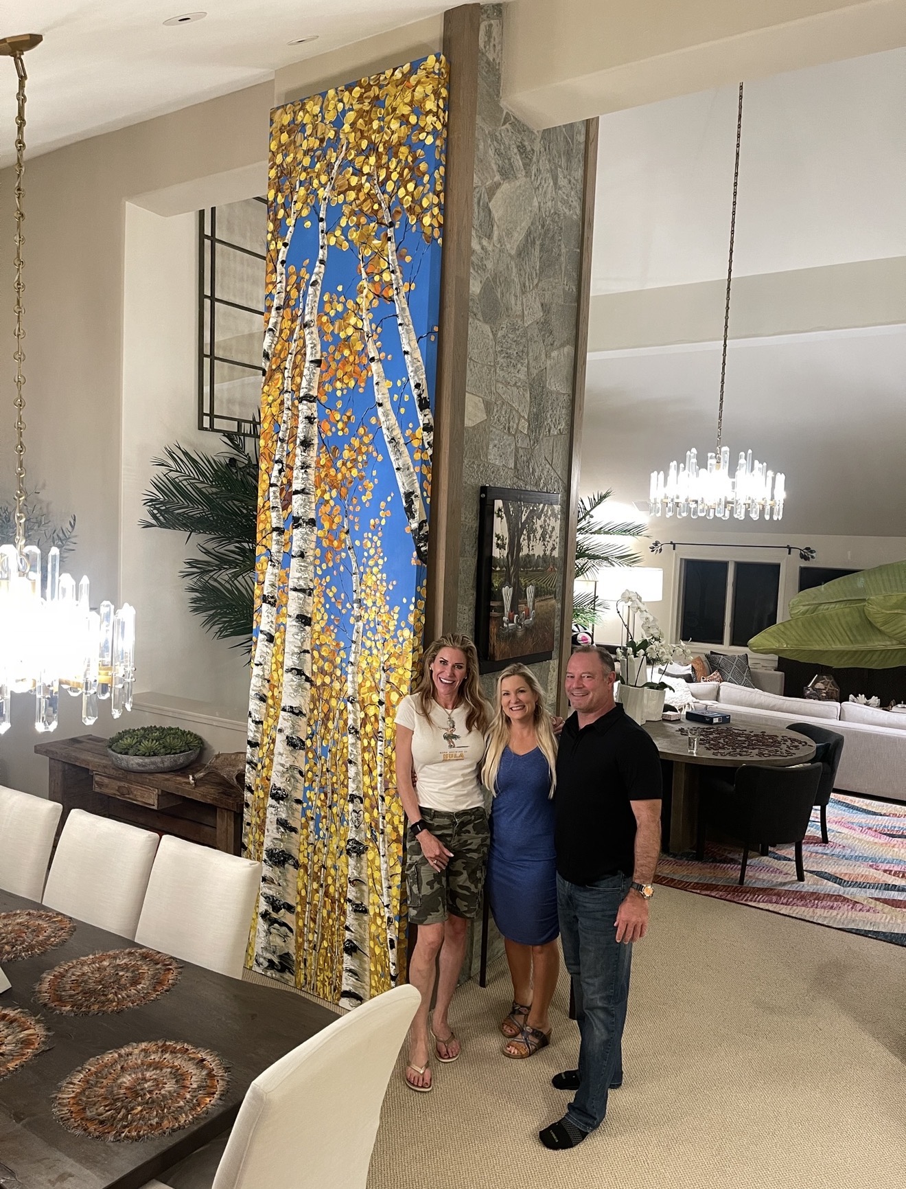 Jennifer Vranes with collectors beside a tall yellow aspen painting in a collector home
